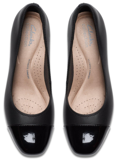 A pair of black cap-toe pumps viewed from directly above, featuring a matte black body and a glossy black patent leather toe cap, with beige insoles marked with 'Clarks Collection' and 'Ultimate Comfort' text.