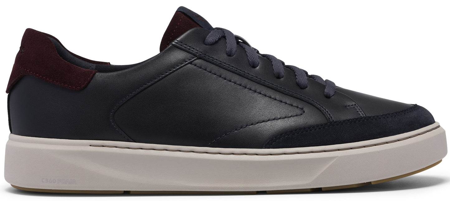 A low-top, black leather sneaker with a rounded toe, featuring dark grey laces, a maroon suede heel tab, a matching maroon tongue, and a thick, beige rubber sole.
