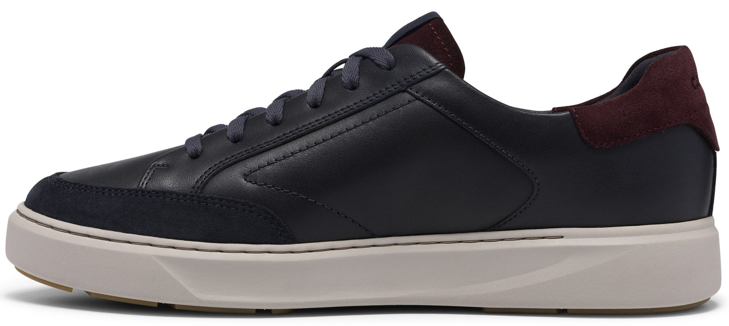 A low-top, black leather sneaker with a dark navy suede toe overlay, a thick cream-colored rubber sole, dark grey laces, and a contrasting maroon suede heel tab.