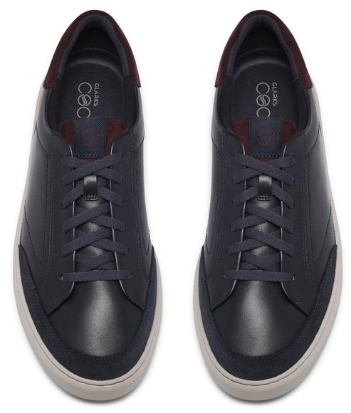 A pair of navy blue leather sneakers viewed from directly above, featuring matching navy laces, a white rubber sole, and a dark burgundy accent on the heel collar.