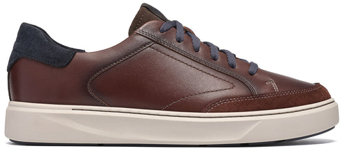A brown leather low-top sneaker featuring a dark navy blue suede heel panel, dark brown suede detailing on the toe, grey laces, and a thick, off-white rubber sole.