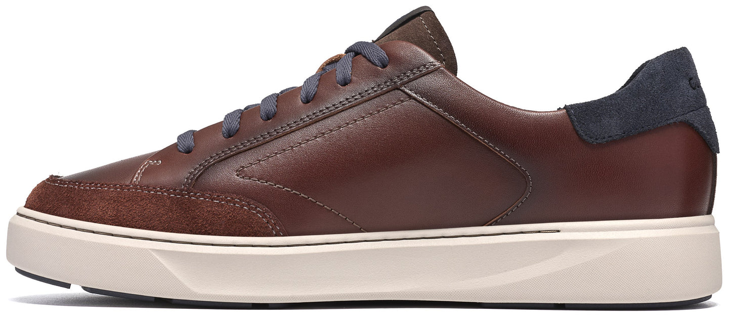 A brown leather low-top sneaker featuring a dark brown suede toe cap, a dark blue suede heel overlay, grey laces, and a thick off-white rubber sole.