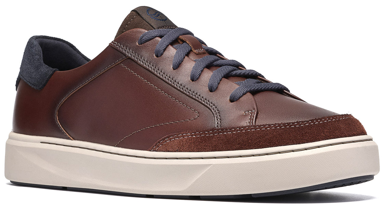 A brown leather low-top sneaker featuring dark blue laces, a dark blue heel counter, and a light-colored, thick rubber sole with a textured suede-like panel at the toe.