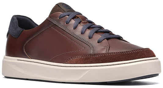 A brown leather low-top sneaker featuring dark blue laces, a dark blue heel counter, and a light-colored, thick rubber sole with a textured suede-like panel at the toe.