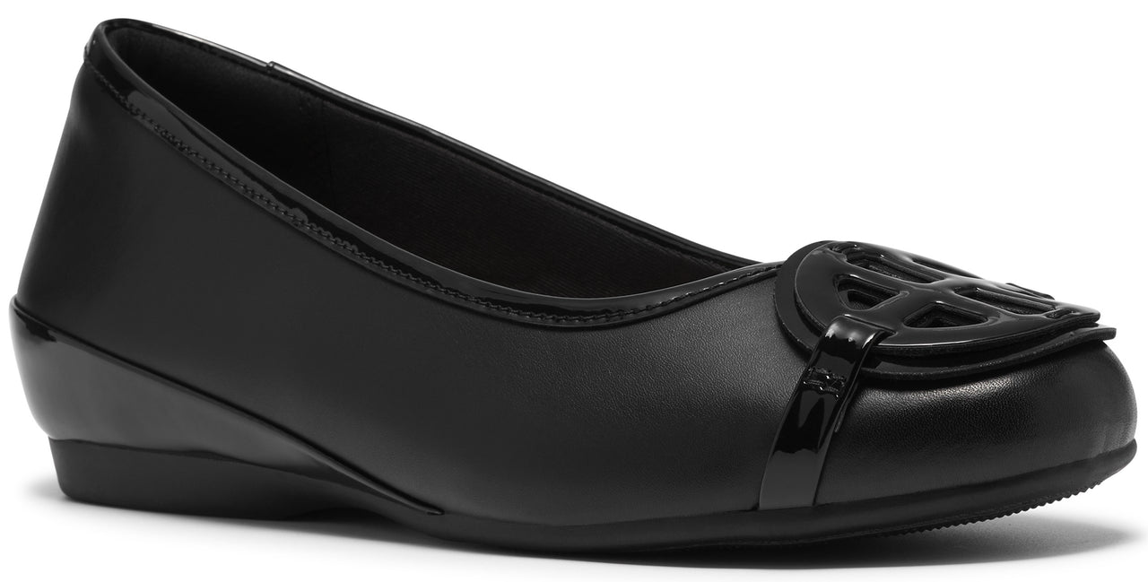 A black slip-on flat shoe with a smooth leather finish and a prominent circular logo cutout ornament on the rounded toe.
