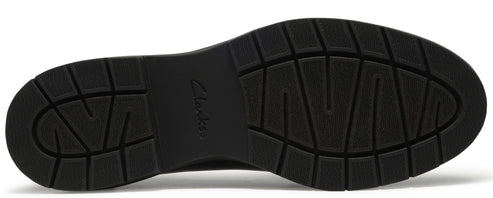 A bottom view of a black shoe sole featuring a tread pattern of textured rectangles and deep grooves with the word Clarks embossed in the center arch.