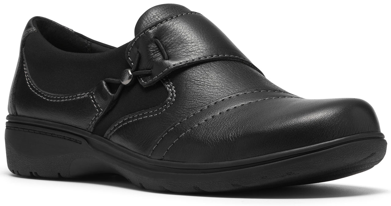 A black leather slip-on shoe with a rounded toe, subtle side stitching detail, and a decorative metallic button near the instep, sitting on a low, matching black rubber outsole.
