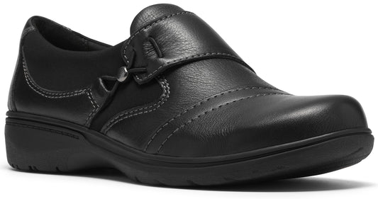 A black leather slip-on shoe with a rounded toe, subtle side stitching detail, and a decorative metallic button near the instep, sitting on a low, matching black rubber outsole.