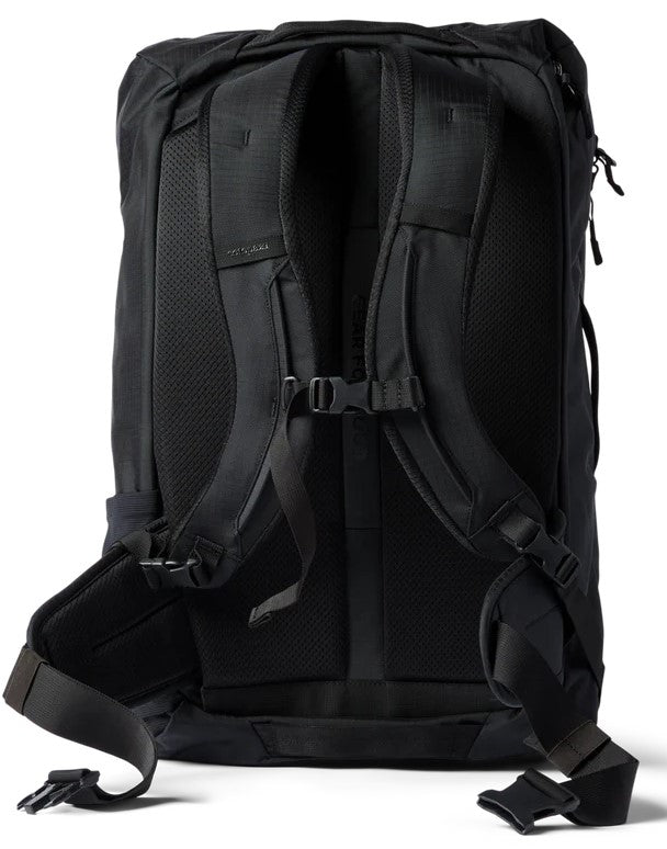 A back view of a solid black travel backpack showing the mesh-padded shoulder straps, an adjustable sternum strap, and a padded hip belt with buckle closures.