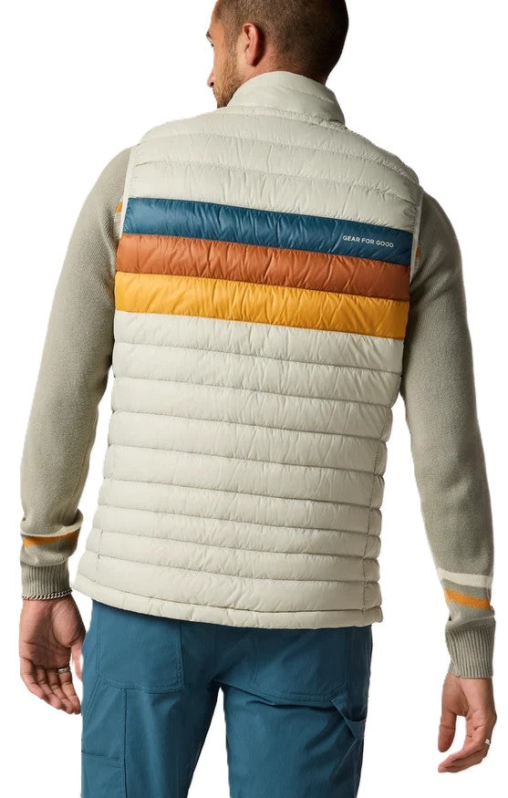 A man seen from behind wearing an off-white puffer vest featuring horizontal stripes of teal, rust, and yellow across the upper back. He is also wearing a coordinating gray long-sleeved sweater with similar stripes on the sleeves, and dark teal pants.
