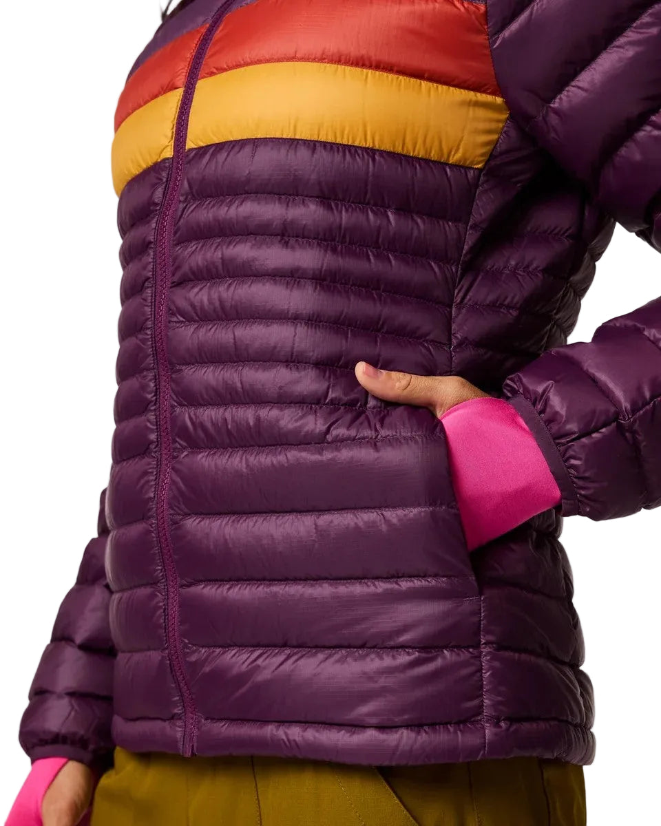A cropped side view of a person wearing a puffer jacket that is dark purple with a horizontal red and yellow stripe across the chest, featuring a hand inside the left pocket and bright pink sleeve cuffs.