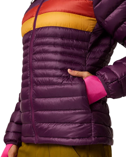 A cropped side view of a person wearing a puffer jacket that is dark purple with a horizontal red and yellow stripe across the chest, featuring a hand inside the left pocket and bright pink sleeve cuffs.