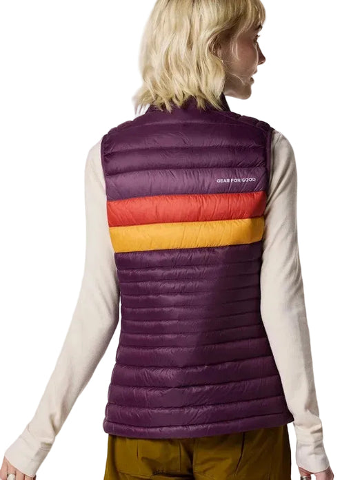 A person viewed from the back wearing a dark purple quilted vest over a long-sleeved light-colored shirt. The vest features horizontal stripes of orange and yellow across the upper back and the text GEAR FOR GOOD printed on the upper right side.