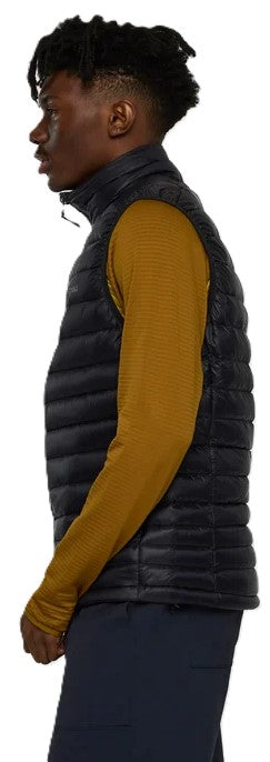 A man in profile wearing a black puffer vest over a mustard-colored long-sleeved shirt.