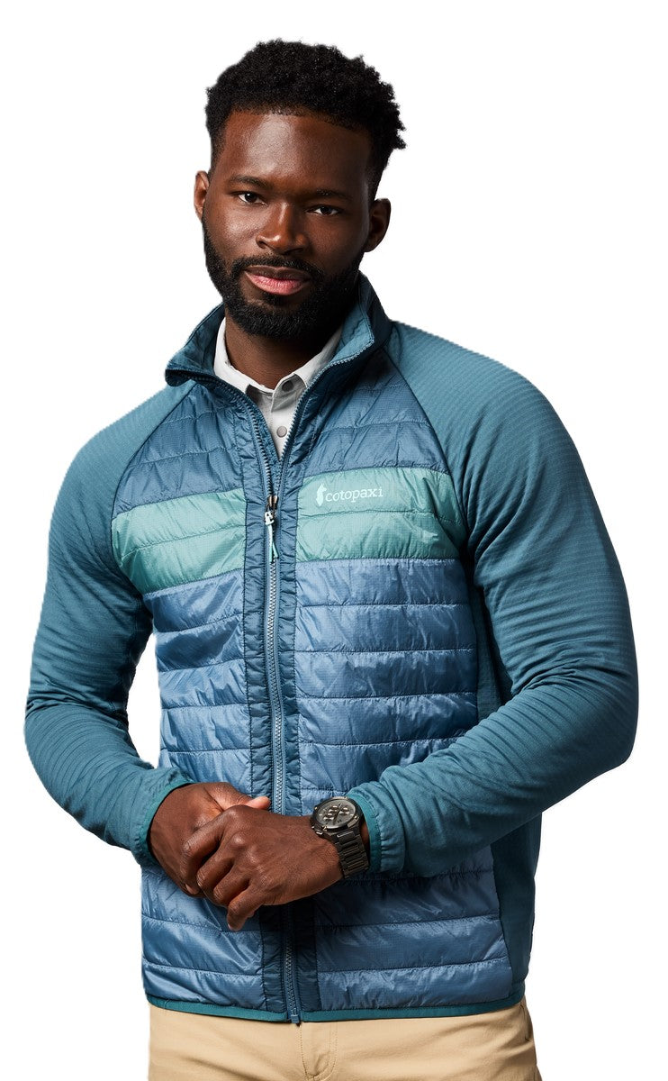 Man in a blue and green quilted jacket with blue raglan sleeves, matching watch, and khaki pants.