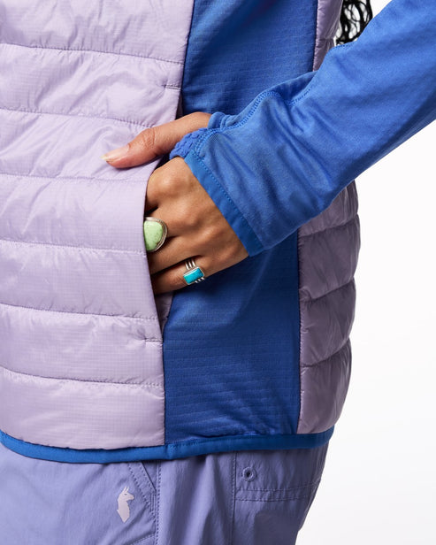 A lilac quilted vest with dark blue trim and panels, worn with a blue long-sleeve shirt; the wearer's hand is tucked in the vest pocket.