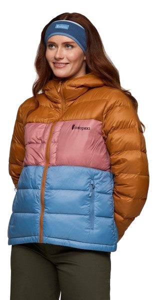 A woman wearing a tan, pink, and blue hooded, down-filled puffer jacket with a blue headband.