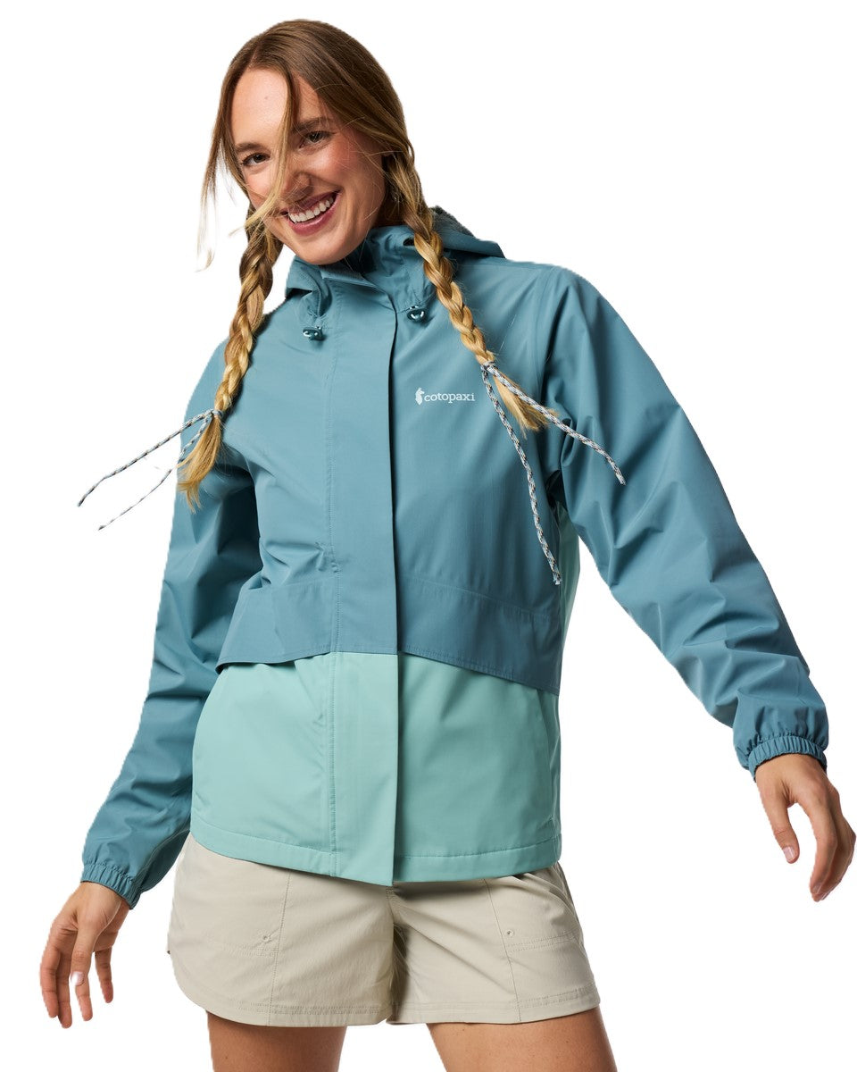 Woman wearing a two-tone teal and green rain jacket with a hood and khaki shorts.