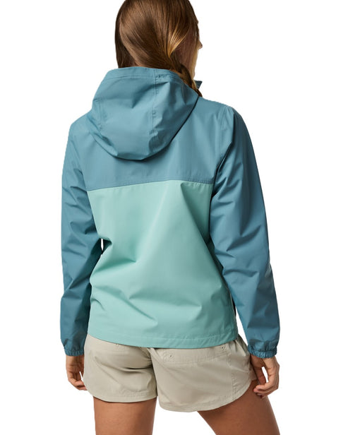 Back view of a woman wearing a teal and mint-green rain jacket with a hood and beige shorts.