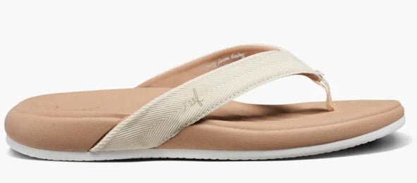 A light tan flip-flop with a white fabric strap featuring a white logo, set on a tan footbed with a white sole.