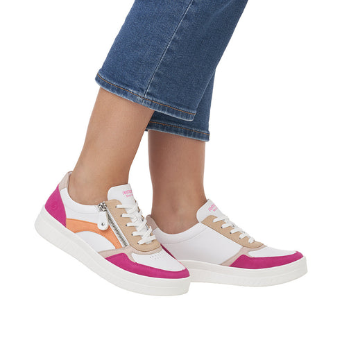 Foot-level view of woman wearing white sneakers with pink and orange accents and side zipper detail.