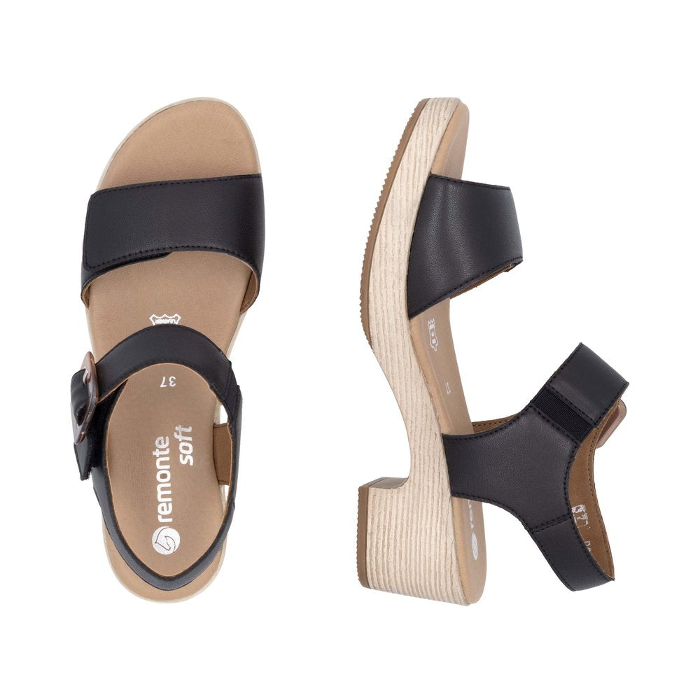 Two black leather sandals, one shown top-down with a strap over the toes and a buckle strap around the ankle, the other shown from the side revealing a low wooden-look heel.