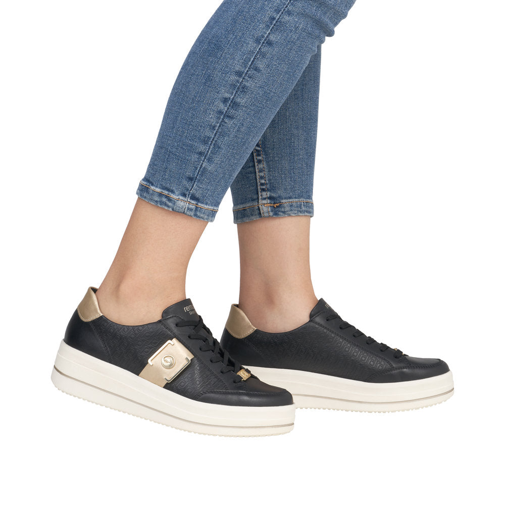 Person wearing jeans and black platform sneakers with metallic gold accents.