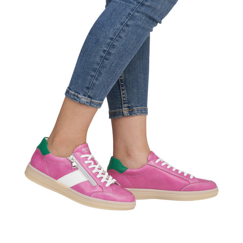 A pair of pink leather sneakers with white laces and a white stripe, worn with rolled up jeans.