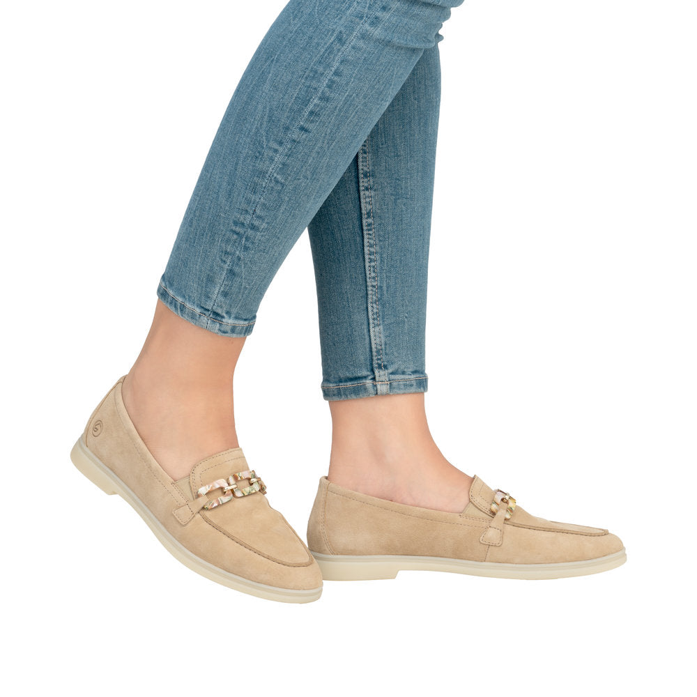 Tan suede loafers with decorative gold buckle, shown on a person wearing light blue denim jeans.