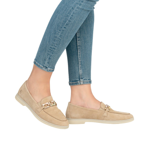 Tan suede loafers with decorative gold buckle, shown on a person wearing light blue denim jeans.