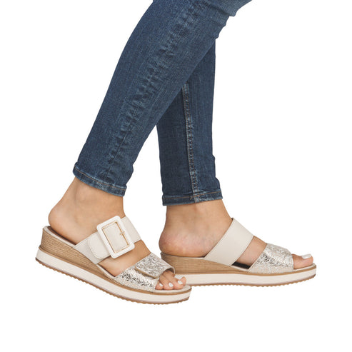 A woman wearing two different off-white wedge sandals with adjustable straps, and a faux snakeskin design.