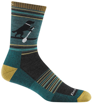 A crew-length hiking sock in teal, charcoal, and mustard yellow featuring a graphic of a black dog standing on a paddleboard on the calf, with a mustard heel and toe and ribbed striped patterning across the foot and ankle.