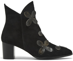 A black suede ankle boot with a block heel, featuring a pointed toe and decorative dark grey leather floral appliqués along the front seam.