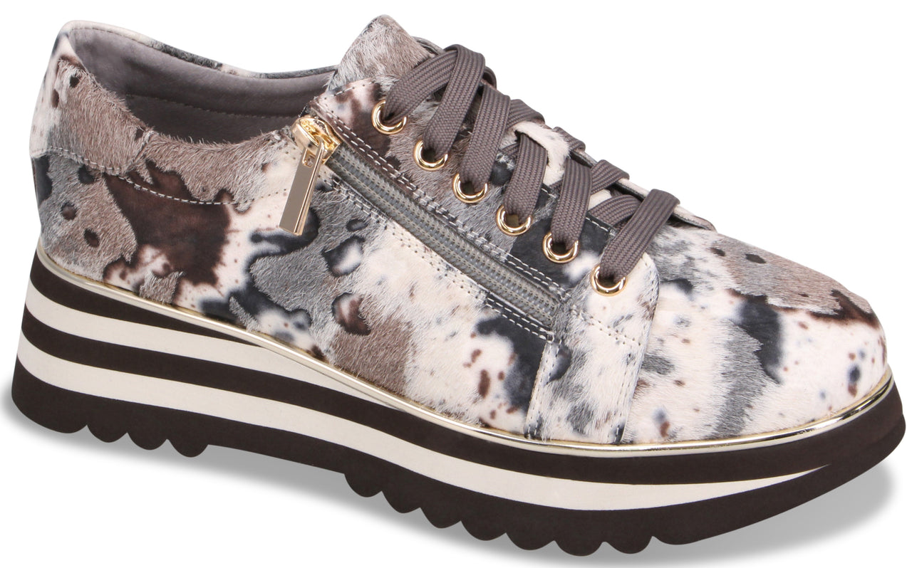 A platform sneaker featuring a multi-colored abstract animal print in shades of grey, black, and white. It has a side zipper closure, grey laces, and a thick, layered sole with a white stripe and a jagged, dark brown tread.