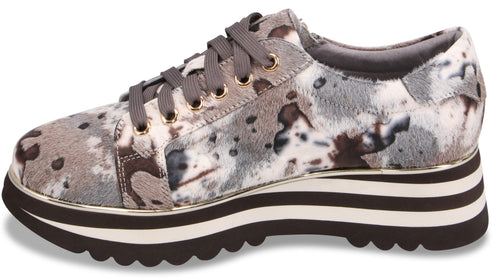 A platform sneaker with a gray and white mottled animal print upper, gray laces, and a thick, layered sole featuring alternating black and white stripes with a gold-tone trim.