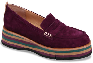 A deep purple suede slip-on loafer with a thick, multi-layered platform wedge sole featuring horizontal stripes in purple, green, and tan.