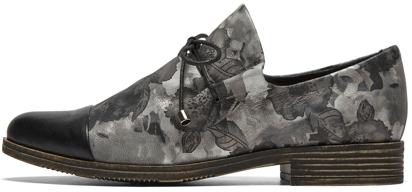 A gray and black floral pattern flat oxford shoe with a smooth black toe cap, thin black laces, and a low stacked wooden heel.