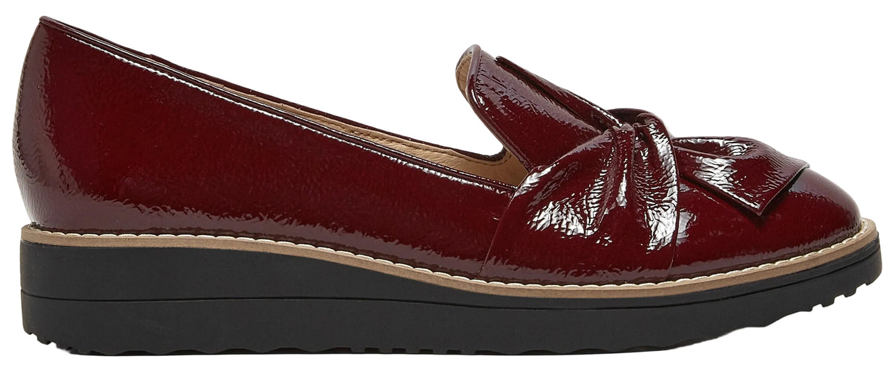 A side view of a maroon-colored patent leather slip-on wedge shoe with a knotted detail on the front and a thick black rubber sole.