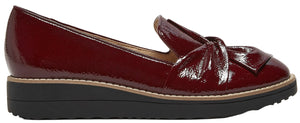 A side view of a maroon-colored patent leather slip-on wedge shoe with a knotted detail on the front and a thick black rubber sole.