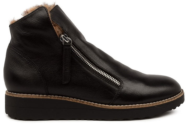 A black leather women's ankle boot with a side zipper closure, a rounded toe, a tan stitched midsole, and a thick black rubber sole with fur lining at the ankle opening.