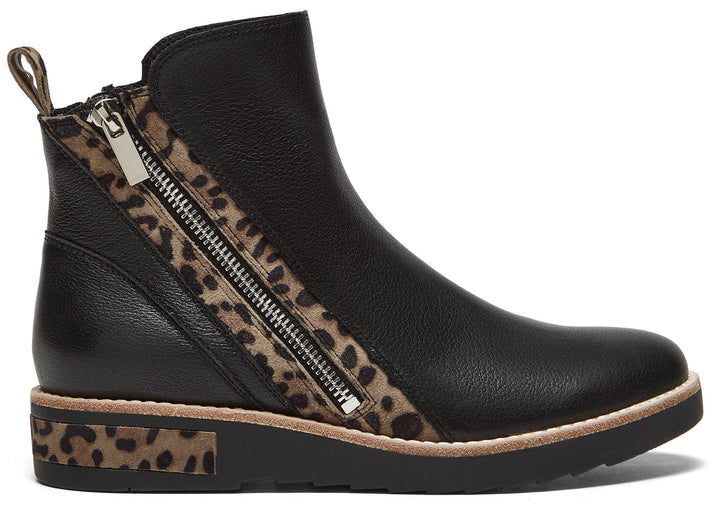 A black ankle boot with a textured leather upper, featuring an asymmetric side zipper framed by a leopard print accent, and a black sole with a leopard print detail on the heel.