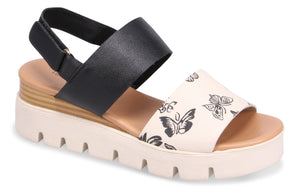 A platform sandal with black elastic heel strap and ivory toe strap adorned with black butterflies.