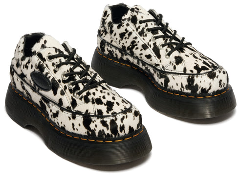 Platform sneakers in white with black cow print, black laces, and thick black soles.