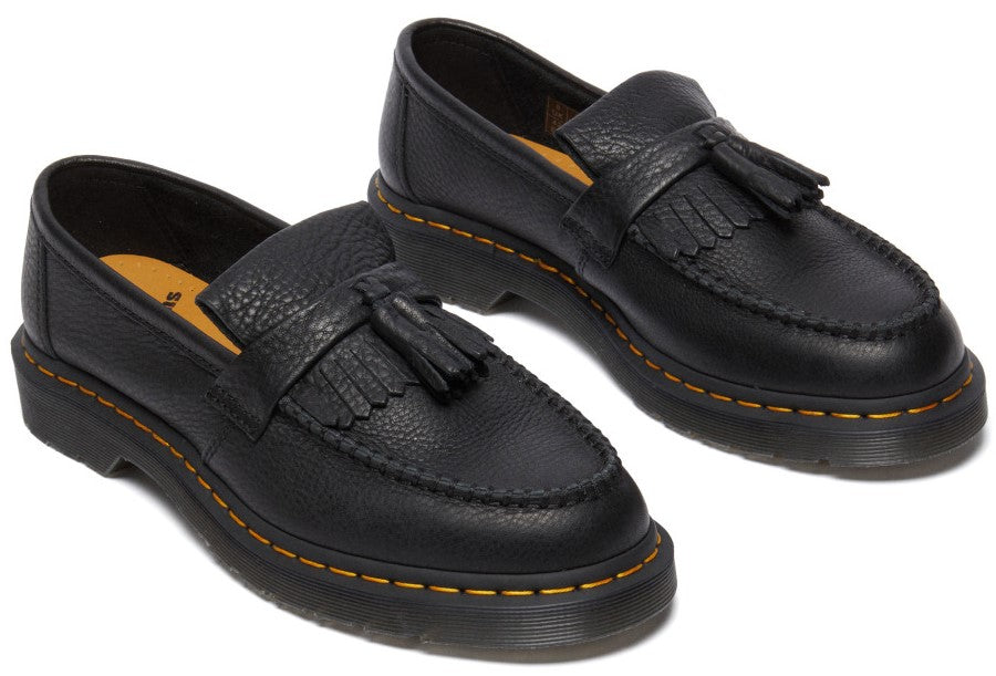 A pair of black pebbled leather tassel loafers with kiltie fringes, featuring a thick lug sole with yellow contrast stitching and gold-colored insoles.