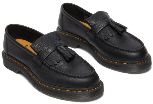 A pair of black pebbled leather tassel loafers with kiltie fringes, featuring a thick lug sole with yellow contrast stitching and gold-colored insoles.