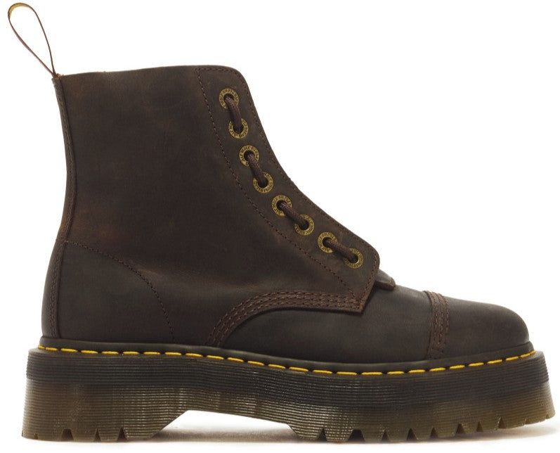 A brown leather ankle boot with a high platform lug sole, yellow stitching around the base, and gold metal eyelets.