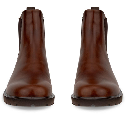 A pair of smooth, brown leather Chelsea boots shown from the front with dark elastic side panels and thick, lugged soles.
