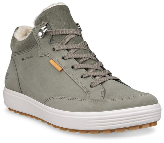 A sage green high-top sneaker with a white midsole, a brown lugged outsole, and white faux fur lining, featuring a Gore-Tex logo on the side, gray laces, and a small orange rectangular tab.