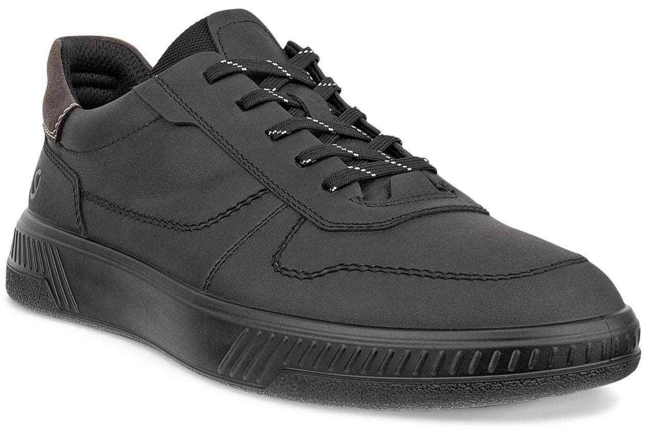 A low-top, matte black leather sneaker with matching black laces featuring thin reflective stripes, a thick black textured rubber sole, and a dark brown padded heel collar.