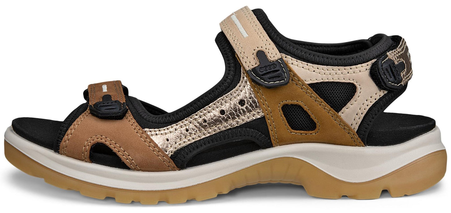 A sandal with tan, black, and gold straps and a thick sole.